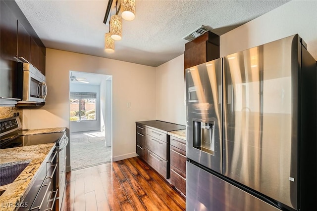 kitchen featuring appliances with stainless steel finishes, hanging light fixtures, light stone counters, dark wood-type flooring, and a textured ceiling