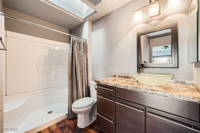 bathroom featuring wood-type flooring, toilet, walk in shower, and a skylight