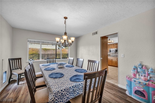 dining area featuring a notable chandelier, a textured ceiling, and light wood-type flooring