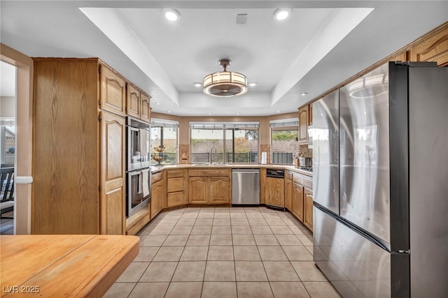 kitchen with light tile patterned flooring, sink, light brown cabinets, a tray ceiling, and stainless steel appliances