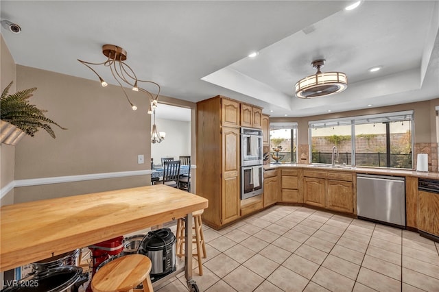 kitchen with sink, light tile patterned floors, stainless steel appliances, a tray ceiling, and decorative light fixtures