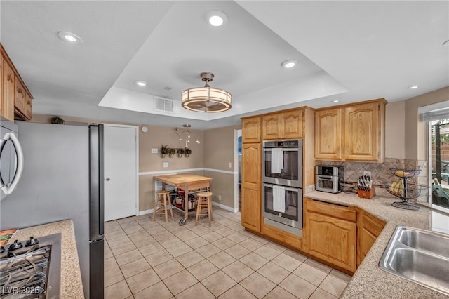 kitchen featuring sink, light tile patterned floors, a tray ceiling, stainless steel appliances, and decorative backsplash