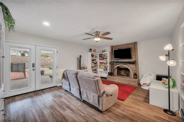 living room with hardwood / wood-style flooring, a brick fireplace, ceiling fan, and french doors