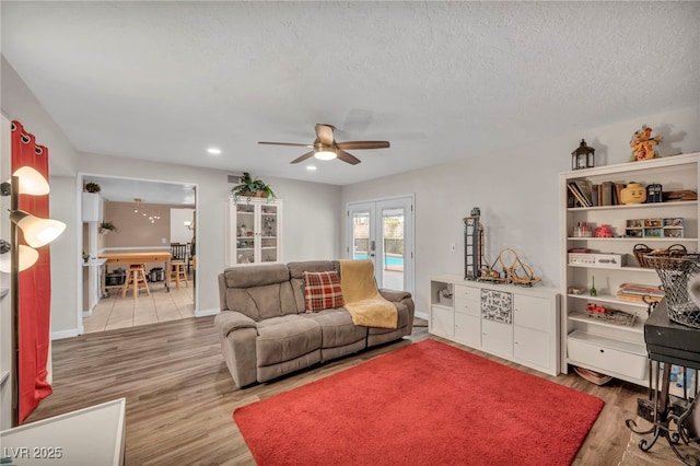 living room featuring ceiling fan, a textured ceiling, light wood-type flooring, and french doors