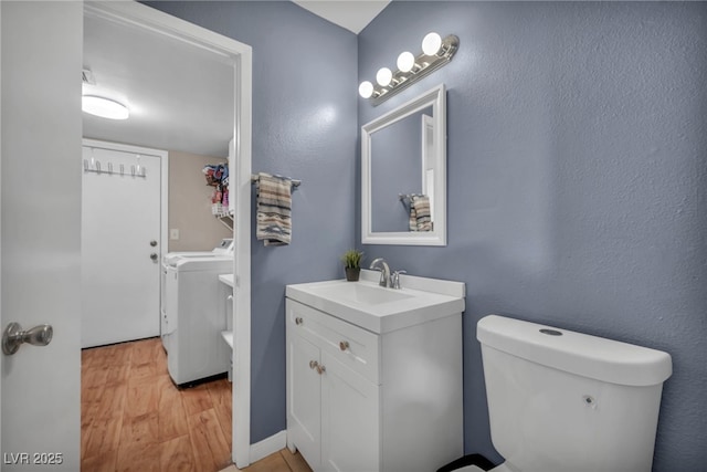 bathroom with washing machine and clothes dryer, vanity, toilet, and hardwood / wood-style floors