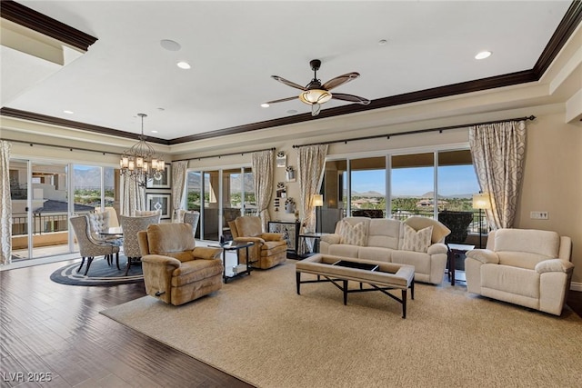 living room with hardwood / wood-style flooring, a tray ceiling, ceiling fan with notable chandelier, and crown molding