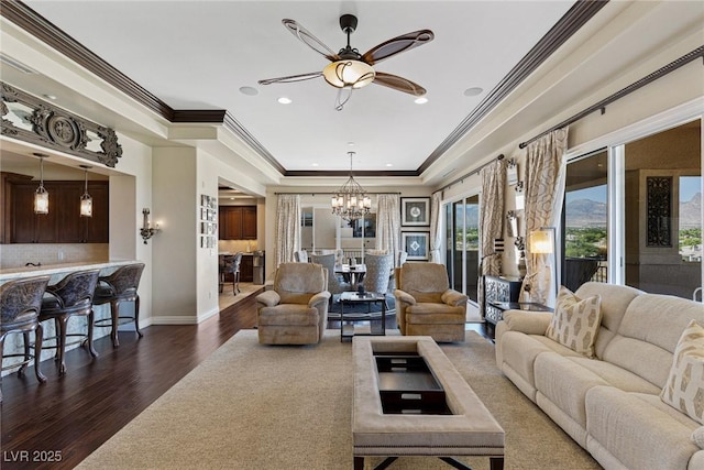 living room with crown molding, dark hardwood / wood-style floors, ceiling fan with notable chandelier, and a tray ceiling