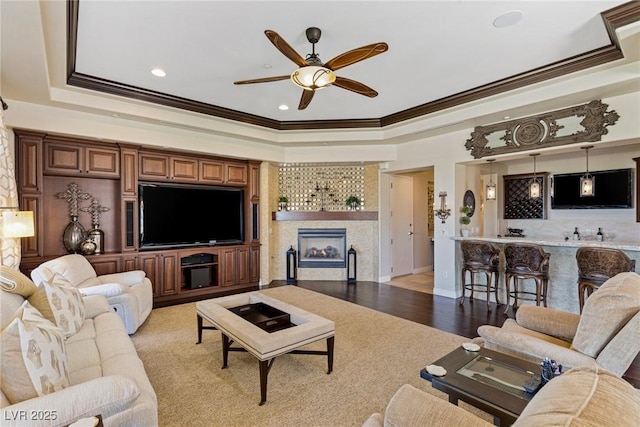 living room featuring a tile fireplace, ornamental molding, and a tray ceiling