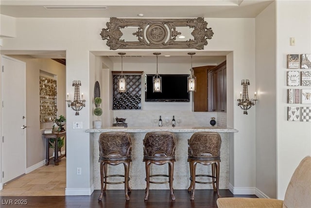 bar featuring wood-type flooring, decorative backsplash, light stone counters, and decorative light fixtures