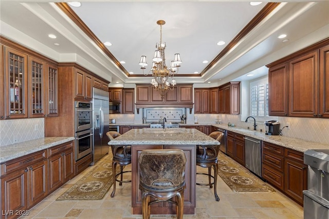 kitchen with sink, a tray ceiling, a kitchen breakfast bar, stainless steel appliances, and a kitchen island with sink