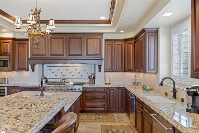 kitchen featuring sink, decorative light fixtures, a tray ceiling, stainless steel appliances, and light stone countertops