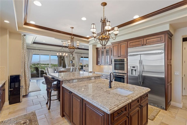 kitchen featuring appliances with stainless steel finishes, a raised ceiling, and a center island with sink