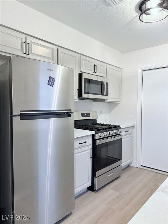 kitchen featuring stainless steel appliances, light hardwood / wood-style floors, and a textured ceiling