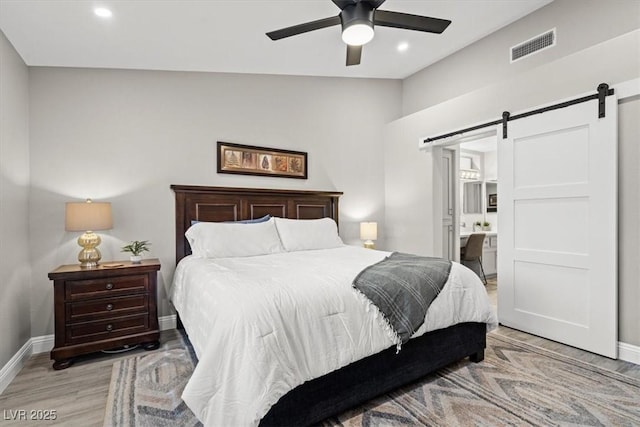 bedroom featuring lofted ceiling, ensuite bath, ceiling fan, a barn door, and light hardwood / wood-style floors