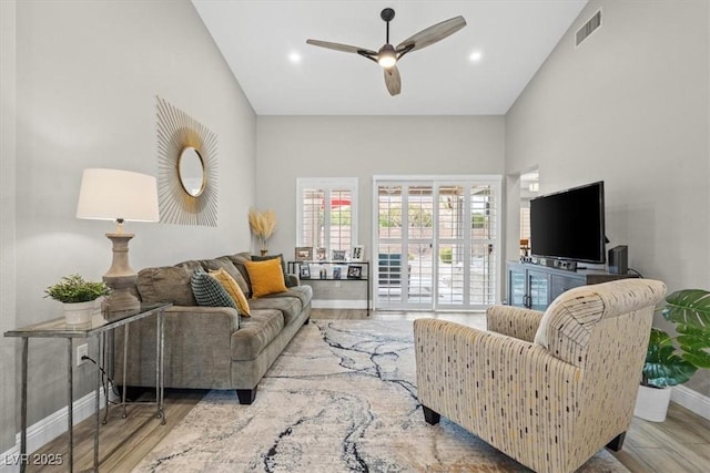 living room featuring a high ceiling, ceiling fan, and light wood-type flooring