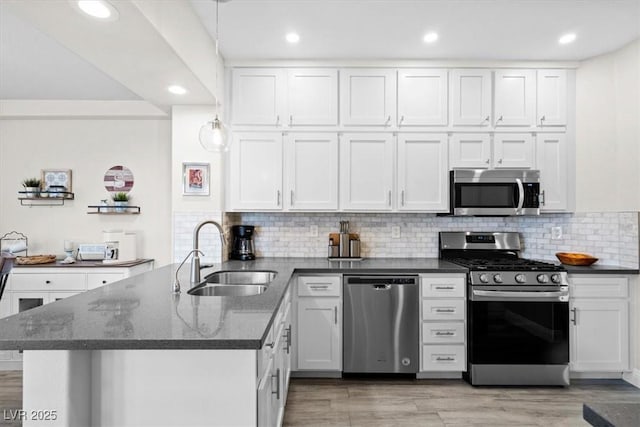 kitchen with sink, appliances with stainless steel finishes, kitchen peninsula, pendant lighting, and white cabinets