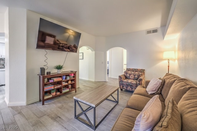 living room with arched walkways, visible vents, light wood-style flooring, and baseboards