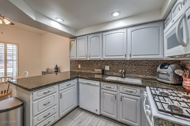 kitchen featuring ceiling fan, a peninsula, white appliances, a sink, and decorative backsplash