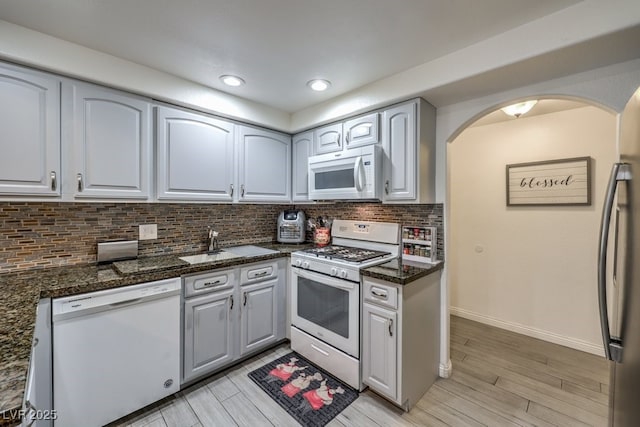 kitchen featuring arched walkways, white appliances, a sink, light wood finished floors, and tasteful backsplash