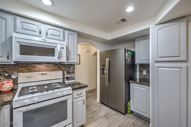 kitchen featuring arched walkways, white appliances, wood finish floors, visible vents, and backsplash