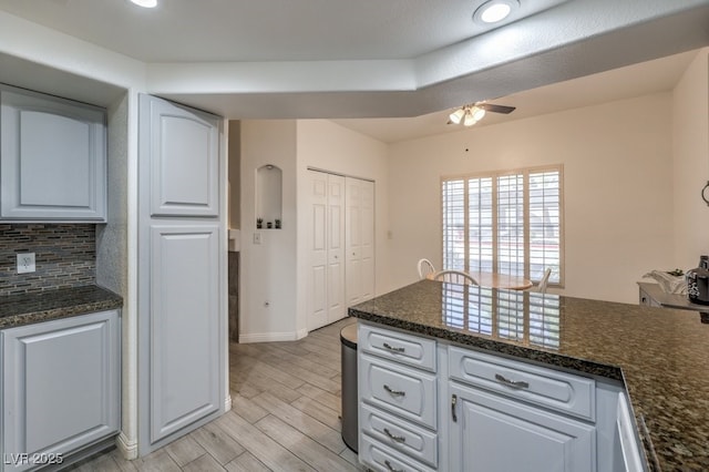 kitchen featuring light wood-style flooring, white cabinetry, a ceiling fan, backsplash, and dark stone countertops