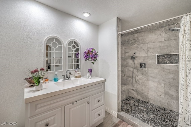 full bathroom featuring a textured wall, wood finished floors, a tile shower, and vanity