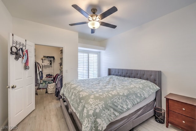 bedroom with light wood-type flooring, a walk in closet, a closet, and a ceiling fan