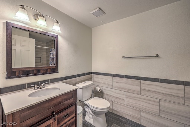 full bath with visible vents, toilet, a shower with curtain, vanity, and tile walls