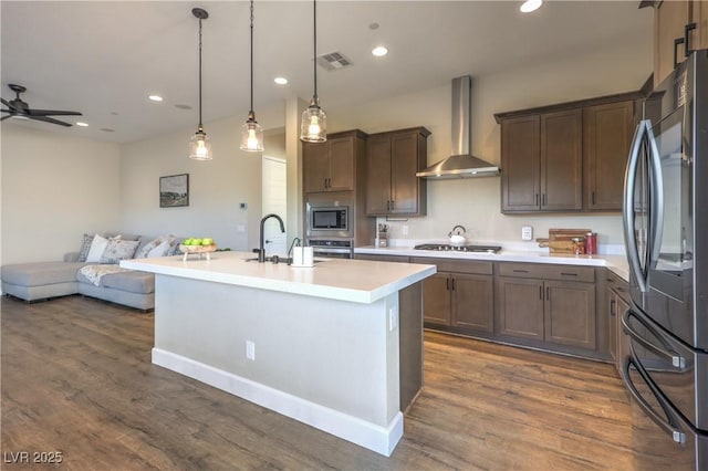 kitchen featuring pendant lighting, sink, stainless steel appliances, a center island with sink, and wall chimney exhaust hood