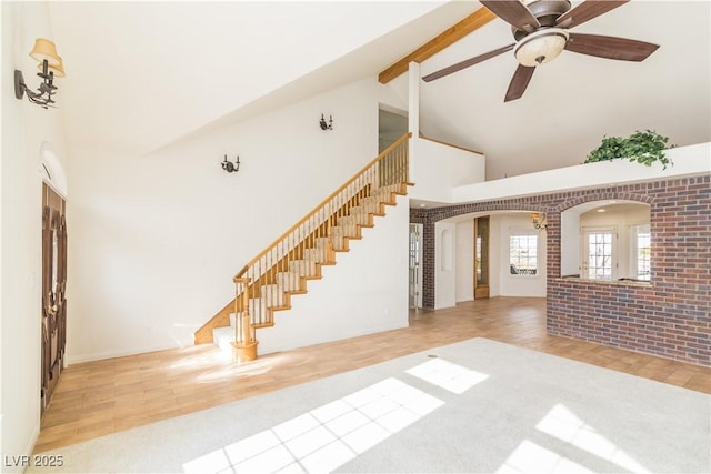 unfurnished living room featuring light tile patterned flooring, high vaulted ceiling, beamed ceiling, ceiling fan, and brick wall