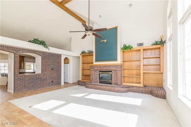 living room featuring high vaulted ceiling, beamed ceiling, ceiling fan, brick wall, and a fireplace