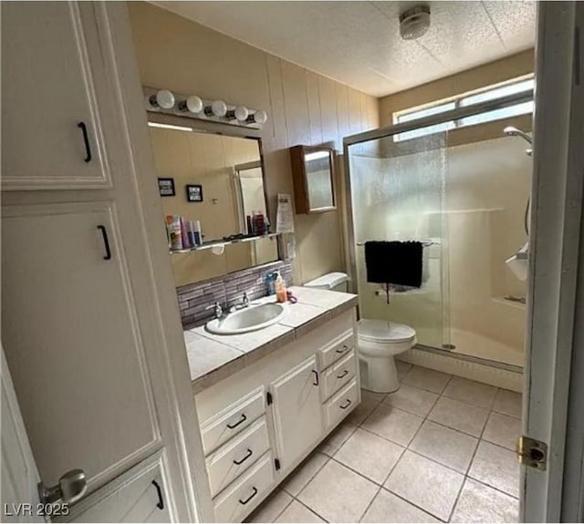 bathroom featuring backsplash, vanity, toilet, a shower with door, and tile patterned floors