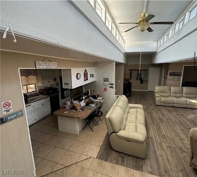 living room featuring sink, light hardwood / wood-style flooring, wooden walls, ceiling fan, and a high ceiling