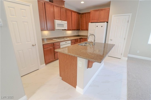 kitchen with a breakfast bar, sink, light stone counters, white appliances, and a kitchen island with sink