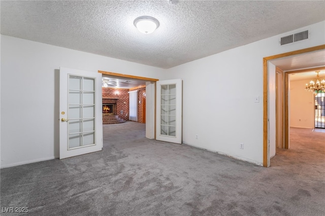 carpeted spare room featuring an inviting chandelier, a brick fireplace, and a textured ceiling