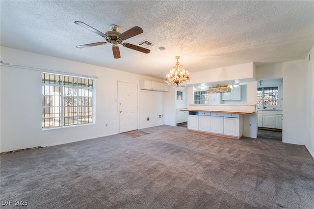 unfurnished living room with dark colored carpet, a wall mounted air conditioner, ceiling fan with notable chandelier, and plenty of natural light