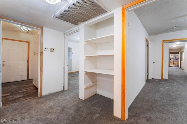 corridor featuring a textured ceiling and dark carpet