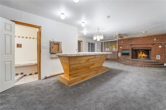 interior space featuring ceiling fan, tile counters, light colored carpet, and a fireplace