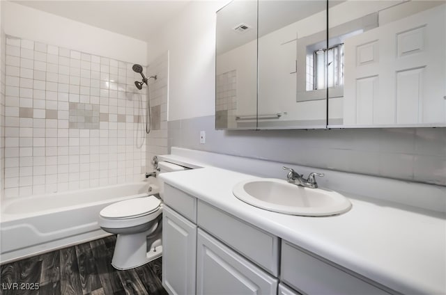 full bathroom with tiled shower / bath combo, vanity, hardwood / wood-style flooring, and toilet