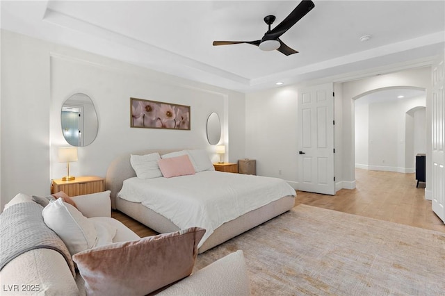 bedroom featuring a raised ceiling, ceiling fan, and light wood-type flooring