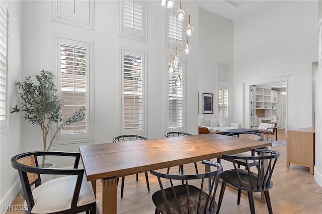 dining area with a wealth of natural light, light hardwood / wood-style floors, and a high ceiling