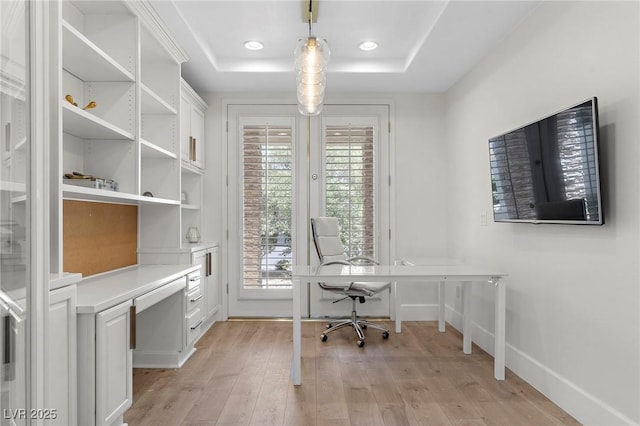 office area with a raised ceiling and light hardwood / wood-style flooring