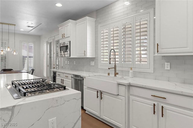 kitchen with sink, decorative light fixtures, stainless steel appliances, light stone countertops, and white cabinets