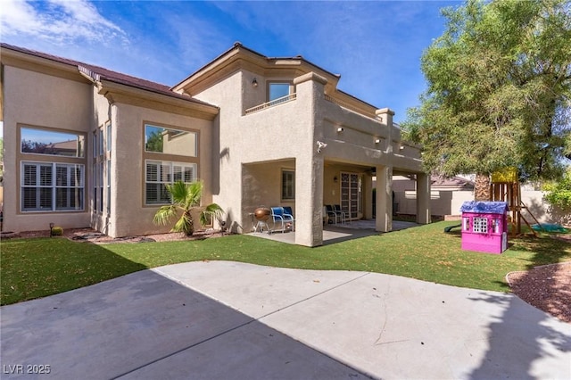 back of property featuring a balcony, a playground, a patio, and a lawn