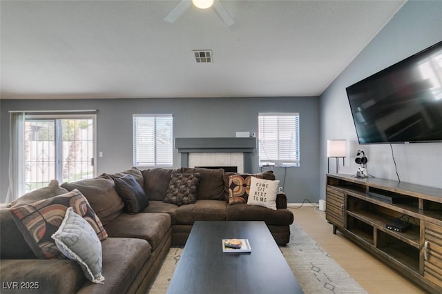 living room with light hardwood / wood-style flooring, a tile fireplace, and ceiling fan