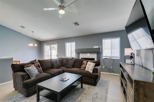 living room with a tile fireplace, lofted ceiling, ceiling fan with notable chandelier, and light hardwood / wood-style flooring