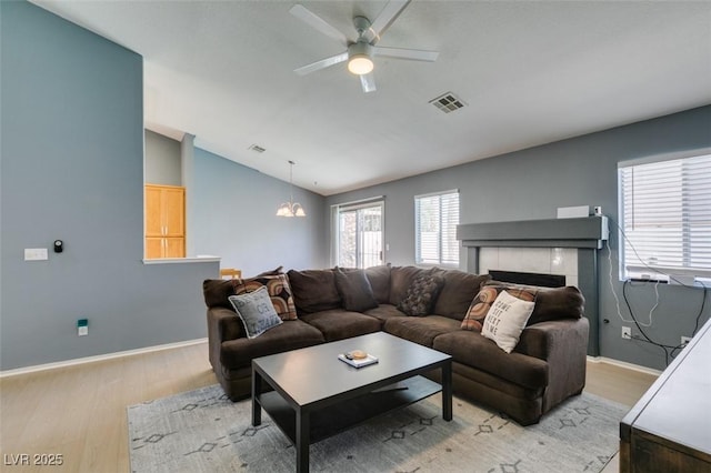 living room featuring lofted ceiling, ceiling fan with notable chandelier, a fireplace, and light wood-type flooring