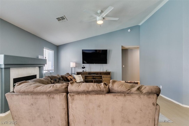 living room with vaulted ceiling, ceiling fan, a tiled fireplace, and light hardwood / wood-style floors