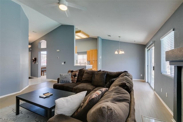 living room featuring vaulted ceiling, a healthy amount of sunlight, ceiling fan with notable chandelier, and light hardwood / wood-style floors