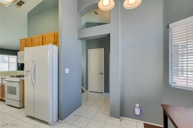 kitchen featuring light tile patterned flooring, white appliances, a towering ceiling, and a wealth of natural light